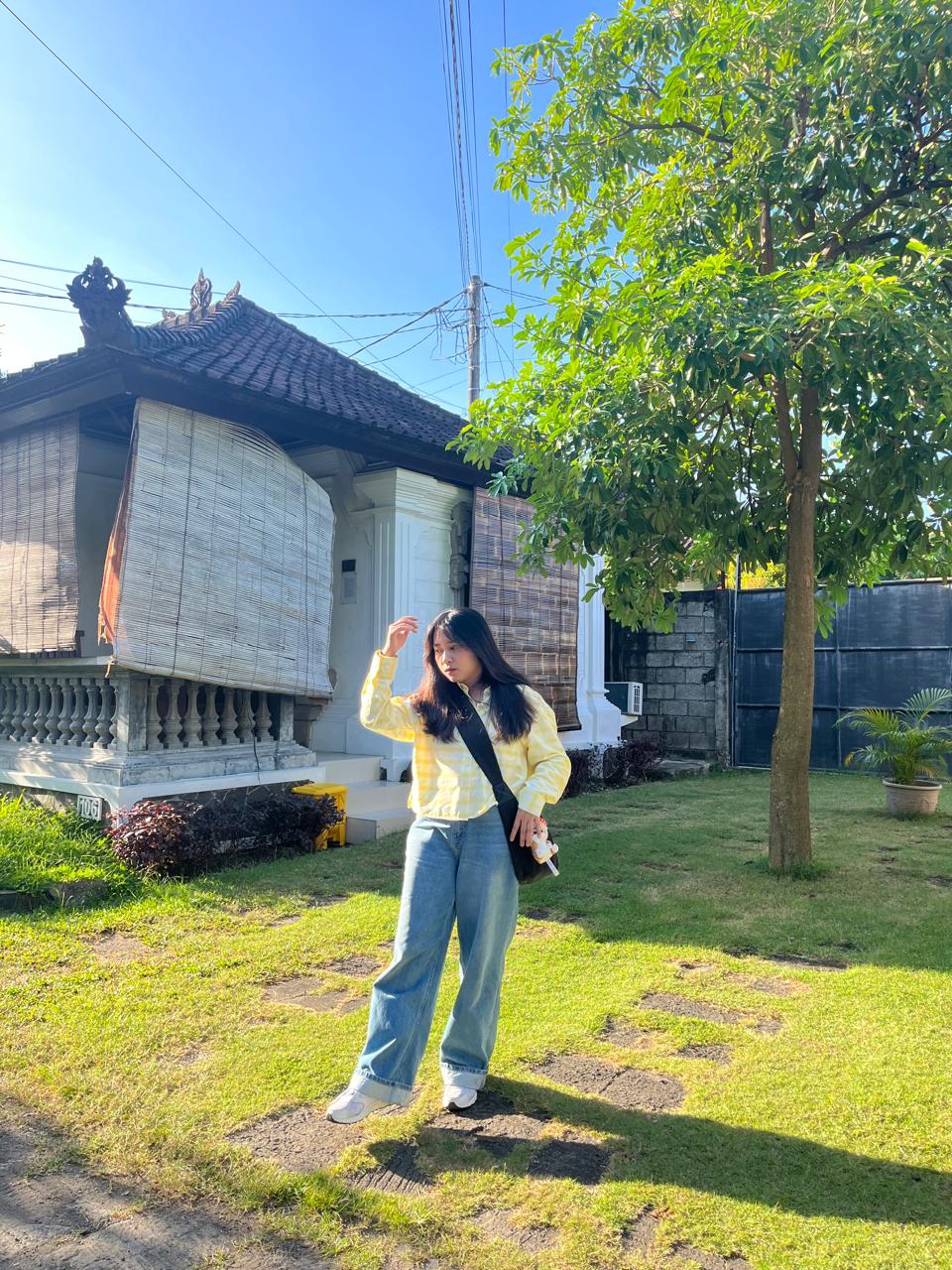 Nia in a yellow shirt outside a traditional house